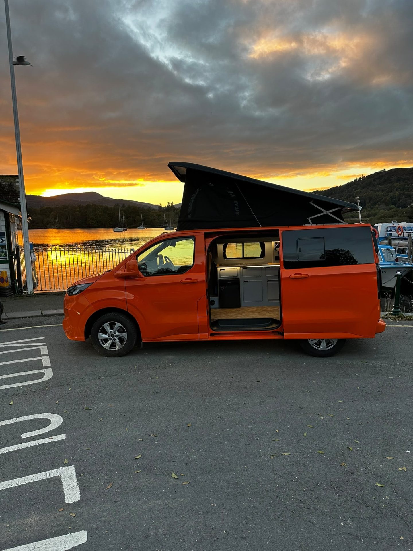 JMC orange pop-top campervan beside a lake at sunset